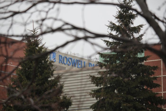 Garrett Looker The Roswell Park building is in the distance. Two evergreen trees in the foreground flank each side of the Roswell sign.